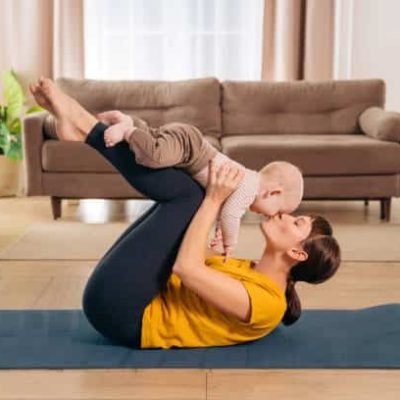Sport with baby. Fit mom kissing her toddler son while holding him on her legs and doing postpartum recovery exercise on fitness mat at home.
Sporty woman exercising together with her little baby